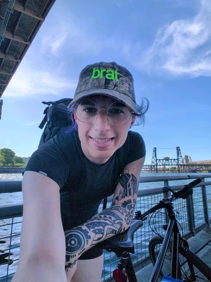 author wearing a hat that says "brat" from Chalie XCX's album at the Portland waterfront with her bike