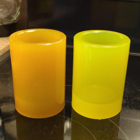 An orange and a yellow storage cup—such as a hefty pencil cup, or a small flower pot— on a well lit dark background.