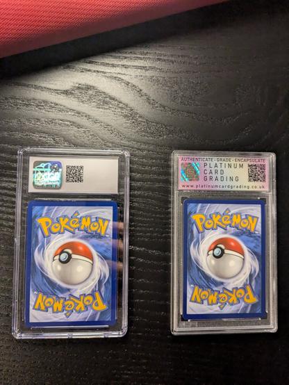 The picture shows two graded Pokémon cards encased in protective slabs from behind.
