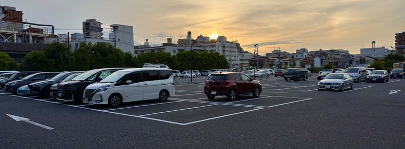 Looking over parked cars in a suburban parking lot in the Itabashi Ward of Tokyo, Japan, the sun is setting in the background.