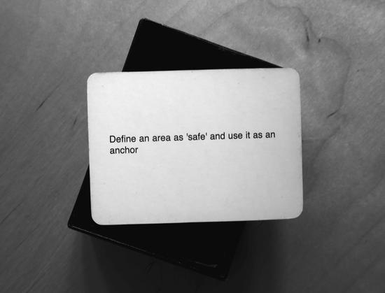 A black-and-white photo of an Oblique Strategy card. The card reads: 'Define an area as 'safe' and use it as an anchor'.