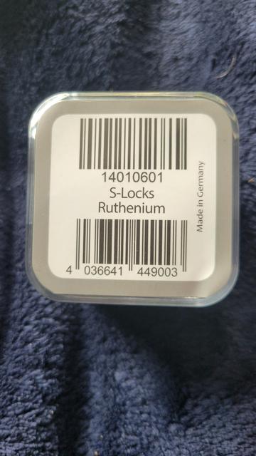 The bottom of the packaging from the previous image. There are 2 barcodes, one at the top, one at the bottom. Between them reads 

14010601
S-Locks
Ruthenium

Below the bottom barcode reads

4 036641 449003

At the right it says "Made In Germany" sideways. 

The background is dark blue and fuzzy.