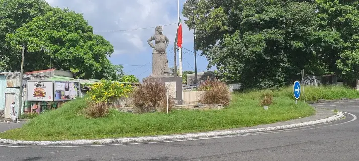 The image depicts a roundabout featuring a statue, surrounded by greenery. The statue appears to be placed in the center of the roundabout, with trees and plants surrounding the area. Flags and signage can be seen nearby, along with some buildings in the background. The overall setting is a mix of urban and natural elements.

Image Credits: Wikimedia / Guallendra / CC BY-SA 4.0