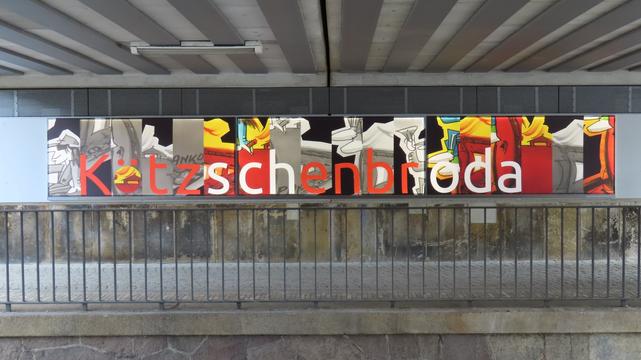 Eisenbahnbrücke. An der Wand ein längliches Bild.

Udo Lindenberg als Comicfigur ganz vorn, in grau.
Das ganze besteht aus einzelnen Bildern, ähnlich A4-Format, in viel größer. 
Die einzelnen Teile stellen, für mich, durcheinander gewürfelte Bildteile eines Zuges, comicartig, dar.

In jedem Teil steht ein Buchstabe am unteren Rand, in rot oder weiß und ergibt 'Kötzschenbroda'.