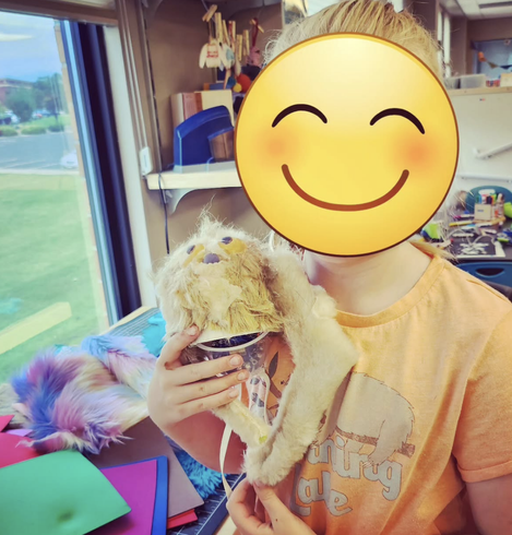Robot camp tween participant holding a companion bot sloth made with a Circuit Playground Express. Her face is obscured by a smiley emoji for privacy.