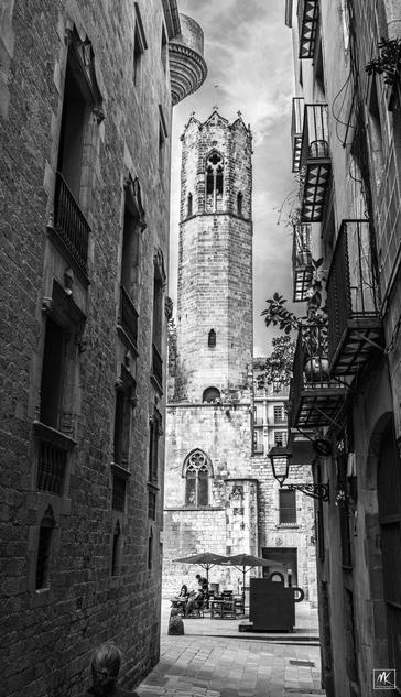 Black and white photo looking down a narrow street framing an octagonal stone tower in the background.