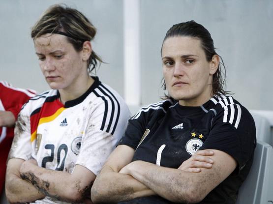 Jennifer Zietz und Nadine Angerer sitzen mit verschränkten Armen in ihren Trikots nebeneinander auf der Spielerinnenbank. Sie haben Regen und Matsch an Armen, Trikots und Gesicht und schauen beide traurig und enttäuscht.