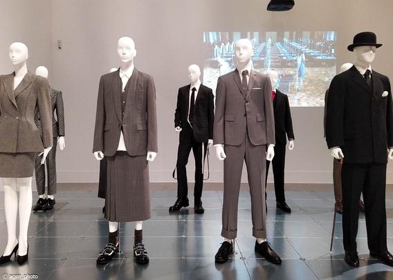 Eine Reihe von Schaufensterpuppen in modischer Straßenkleidung steht auf einem Podest in einer Ausstellungshalle. /
A row of mannequins in fashionable street clothes stand on a pedestal in an exhibition hall.