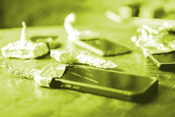 image of 4 smartphones on a table, each with a tiny aluminum-foil hut. the image has a yellow coloring – kind of matching the yellow festival color.
