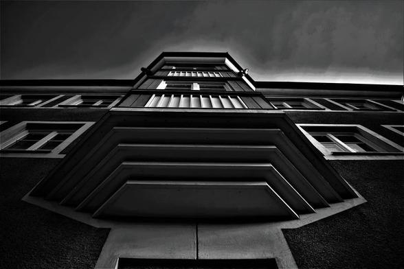 Monochrome photo of a building taking from the ground upwards against the wall and sky