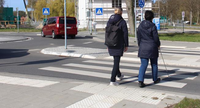 Zu sehen sind sind zwei getrennte Bereiche an einem Fußgängerüberweg. Links für Rollstuhlfahrende mit 0 cm Borsteinkante und Sperrfeld, rechts für Blinde mit Bordsteinkante. Beide Bereiche sind etwa 1,5 Meter breit.