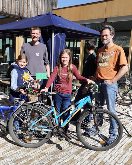 Bild mit 4 Personen: Im Hintergrund zwei Ehrenamtliche des Werkstatt-Cafés, im Vordergrund zwei jugendliche Geschwister, die uns die 1000. Reparatur, ein Fahrrad, gebracht haben.
