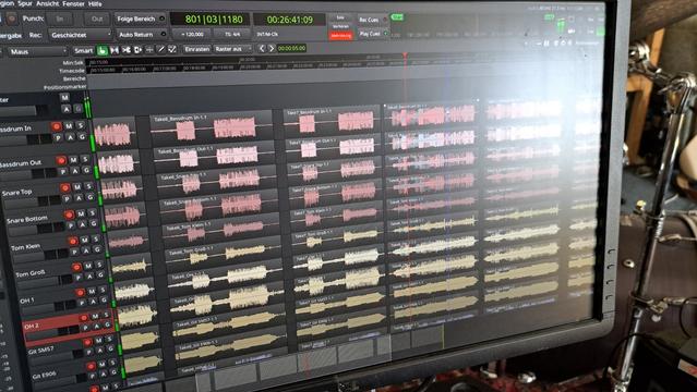 We see a computer screen. It displays a digital audio workstation with a lot of tracks and waveforms in various colors.