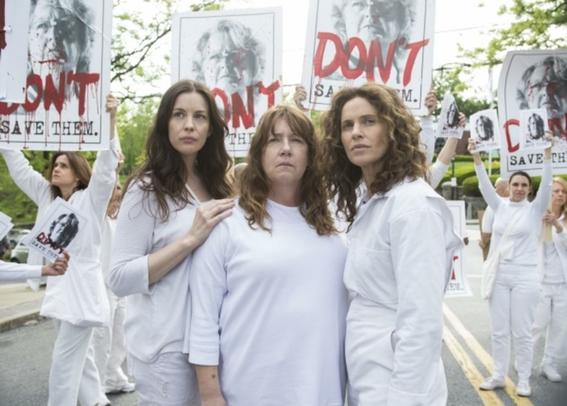 Screenshot of the TV show "The Leftovers" - showing cult members in white with odd signs.