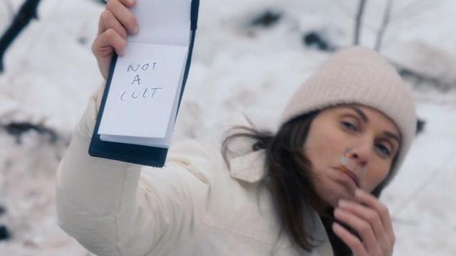 Screenshot of the TV show "The Leftovers" - showing a silent cult member holding up a note saying "not a cult".