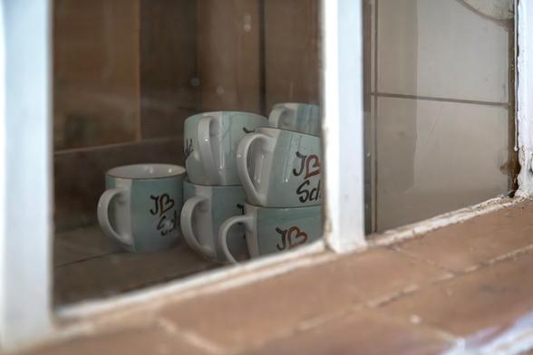 Hinter einem Fenster stehen in einer Art Vitrine sechs türkisfarbene Kaffetassen mit dem Aufdruck I und einem Herz für ich liebe. Danach folgt ein Wort, von dem nur Sch zu erkennen ist. Bis auf die Kaffeetassen sieht alles etwas heruntergekommen aus.