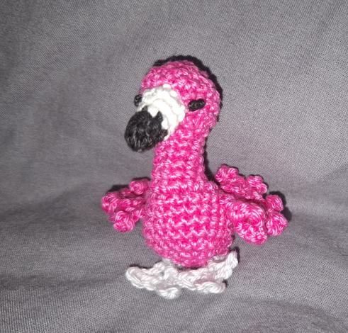 Kleiner pinker, selbstgehäkelter Flamingo auf grauem Grund.