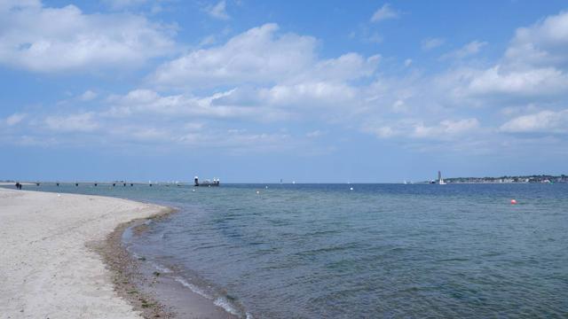 Ein Bild vom Strand, blaues Wasser, blauer Himmel mit weißen Wolken.