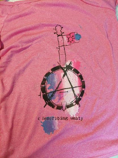 The pink shirt from before, but from the other side. Here, there is a print of a banjo, with a circle A drawn on the banjo head, and a backdrop of colour spats printed as a trans flag.