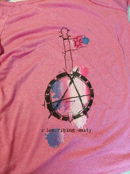 The pink shirt from before, but from the other side. Here, there is a print of a banjo, with a circle A drawn on the banjo head, and a backdrop of colour spats printed as a trans flag.