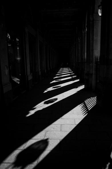 Das Foto zeigt einen Gang der fast komplette dunkel ist, von schräg rechts scheint Sonne durch Säulen und zeichnet helle elliptische Flecken auf die Erde. Es entsteht eine Linie durch die hellen Stellen.