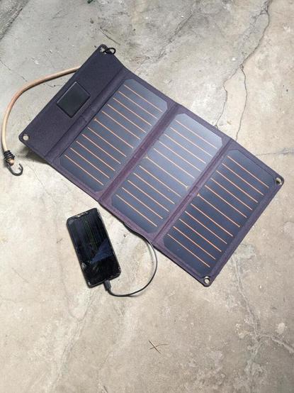 A photo of the compost.party setup. A solar panel plugged into a smartphone