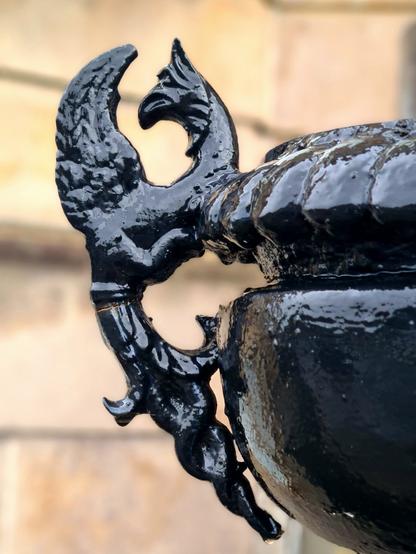 A small dragon-like creature forming the handle to a decorative cast-iron urn.