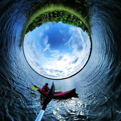 One of a series of photographs in which two people are pictured hiking, biking, and kayaking throughout a beautiful and verdant state park in central Minnesota under cloudy blue late-summer skies.