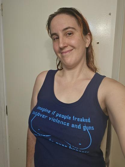 Photo of me smiling with wet hair while wearing my dark blue shirt with a decal of cartoon breast on it that says "imagine if people freaked out over violence and guns the way they do over breasts"