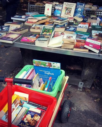 Das Foto entstand beim BookCrossing Picknick in Aachen in 2018.
Eine Tischtennisplatte ist ausgelegt mit sehr vielen Büchern. Davor steht ein Bollerwagen, der ebenfalls mit Büchern gefüllt ist. Diese sind in zwei großen Plastikboxen darin untergebracht.
Die Auswahl reicht von Kinderbüchern über Ratgeber zu allem anderen. Outlander und Buffy sind ebenso vertreten wie "Das Rad der Zeit" oder "Der Ruf der Wildnis".