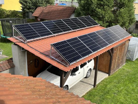 Dvě řady fotovoltaických panelů na plechové střeše přístřešku.