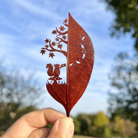 a cut leaf artwork of a squirrel under a tree