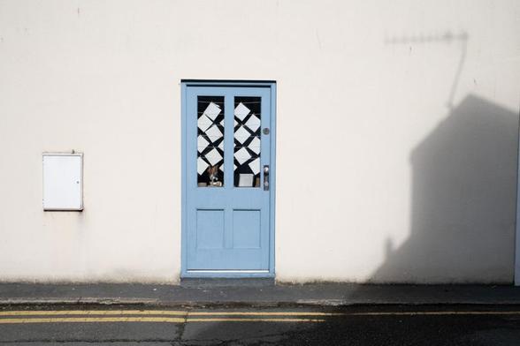 Light blue shop back door (with a two-pane window with diamond-shaped pieces of paper stuck to the reverse) with shadow of building opposite.