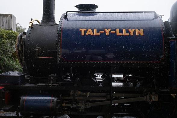 The boiler side of a shiny blue-painted steam locomotive with painted name 'Tal-y-llyn' (also the name of the whole railway).