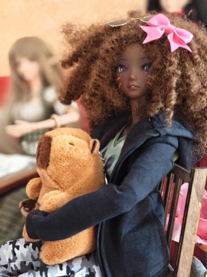 A black Smart Doll with curly hair holding a capybara plushie.