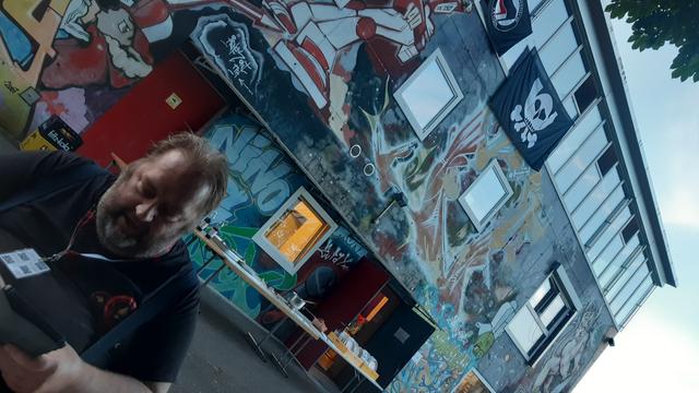 Ein Mensch sitzt vor einem angesprayten Gebäude mit Chaos Post und Antifa Fahne.