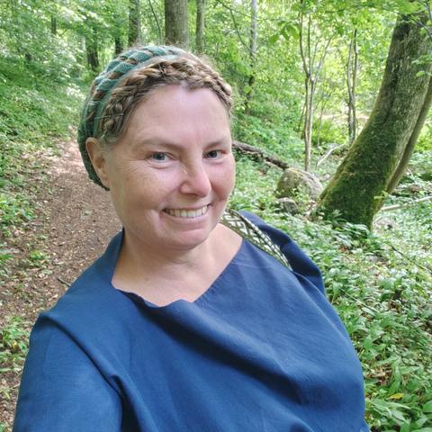 The head and busy of a white middle aged woman in a blue wool tunic, walking in a beech wood.