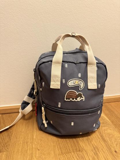 Blaugrauer Kinderrucksack mit aufgenähter Schildkröte, mit Sprechblase, die "Munch" sagt. Am Reißverschluss hängt ein Spiderman-Schlüsselanhänger.