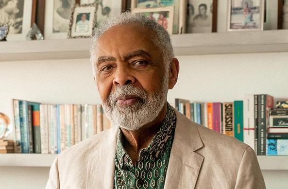 Gilberto Gil, de paletó de linho, em frente a uma estante de livros