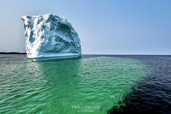 Un gigantesque iceberg en forme de paquebot dérive dans une eau sombre. Autour de lui une tablette immergée, comme s'il était posé sur une soucoupe, donne à l'eau un aspect vert émeraude. Les autres 90% de sa masse ne sont pas visible.