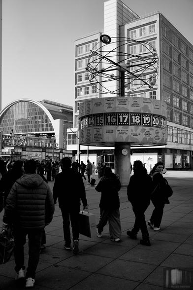 Monochrome street photography in front of the world time clock on Berlin's Alexanderplatz.