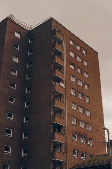 A yellow/red brick tower block, with film grain, and a greyish sky behind