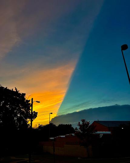 A view of the sky where there is a clear 45º dividing line between an area lit by the setting sun, on the left, and one where the sunlight is blocked by storm clouds, on the right. To the left, the sky and clouds are an eggy yellow. To the right of the line, the sky is a deep blue green.