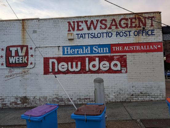 Photo of the side of a brick building painted white with "TV Week" and "New Idea" advertisements painted on the side in a 1990s font.