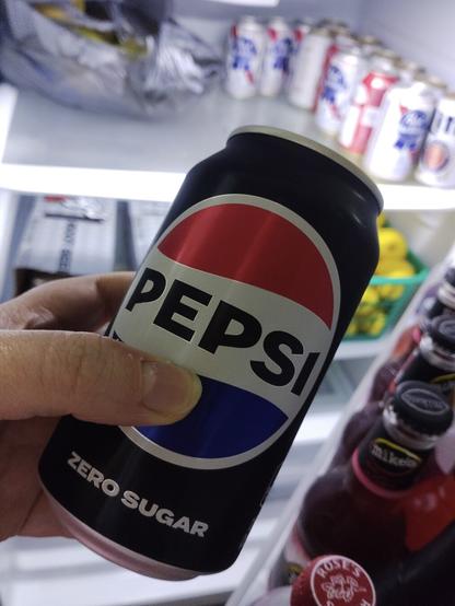Grabbing a soda from the fridge in the garage. Holding a Pepsi zero sugar tilted to the right in line with the open door. The tops of hard lemonade bottles line the shelves on the door. Various canned beers are clustered on the top shelf inside the lit fridge. Shot with a Light Phone III.