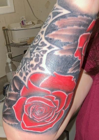 The inside of my forearm, where the roses and the bat continues and how the sleeve overlaps.
PD: Forearm tattoo featuring a large, bold red rose as the central element. The rose petals are richly colored in vibrant red with white highlights along the edges, creating a striking contrast and giving the flower a three-dimensional, almost glowing effect. Surrounding the rose are intricate black and gray patterns, including swirling filigree and web-like designs that add complexity and depth. The background is heavily shaded in black and gray, with some areas blending into softer, smoky gradients, making the red of the rose stand out even more. The overall vibe of the tattoo is dramatic and intense, with a mix of elegance from the ornamental patterns and a sense of mystery from the dark shading. The design feels bold and expressive, with a touch of gothic or romantic flair.