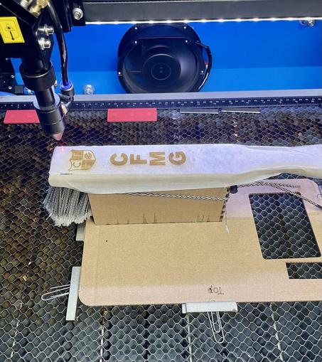 Picture of the laser bed with the engraved bench brush. The brush is held in a cardboard holding jig.