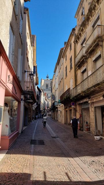 Une rue de Villefranche de Rouergue un jour de marché, on voit des piétons et au loin le donjon de la collégiale