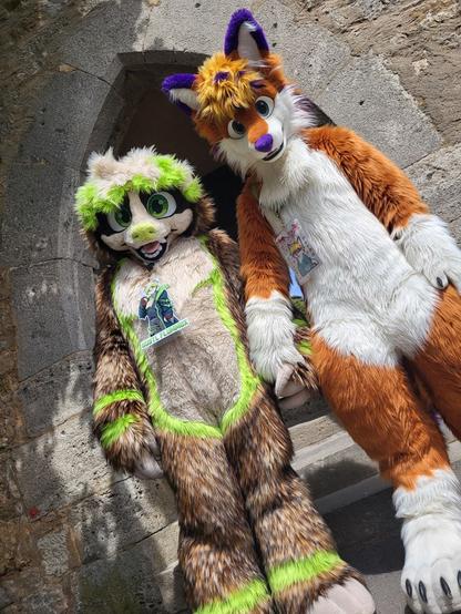 Fursuiters Gustl and Fox Flummox in a dutch angle shot in front of a gothic archway. They're holding paws.
