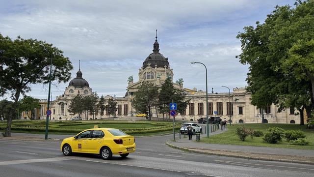 A building with a large dome and ornate architecture, surrounded by green trees and landscaped gardens.